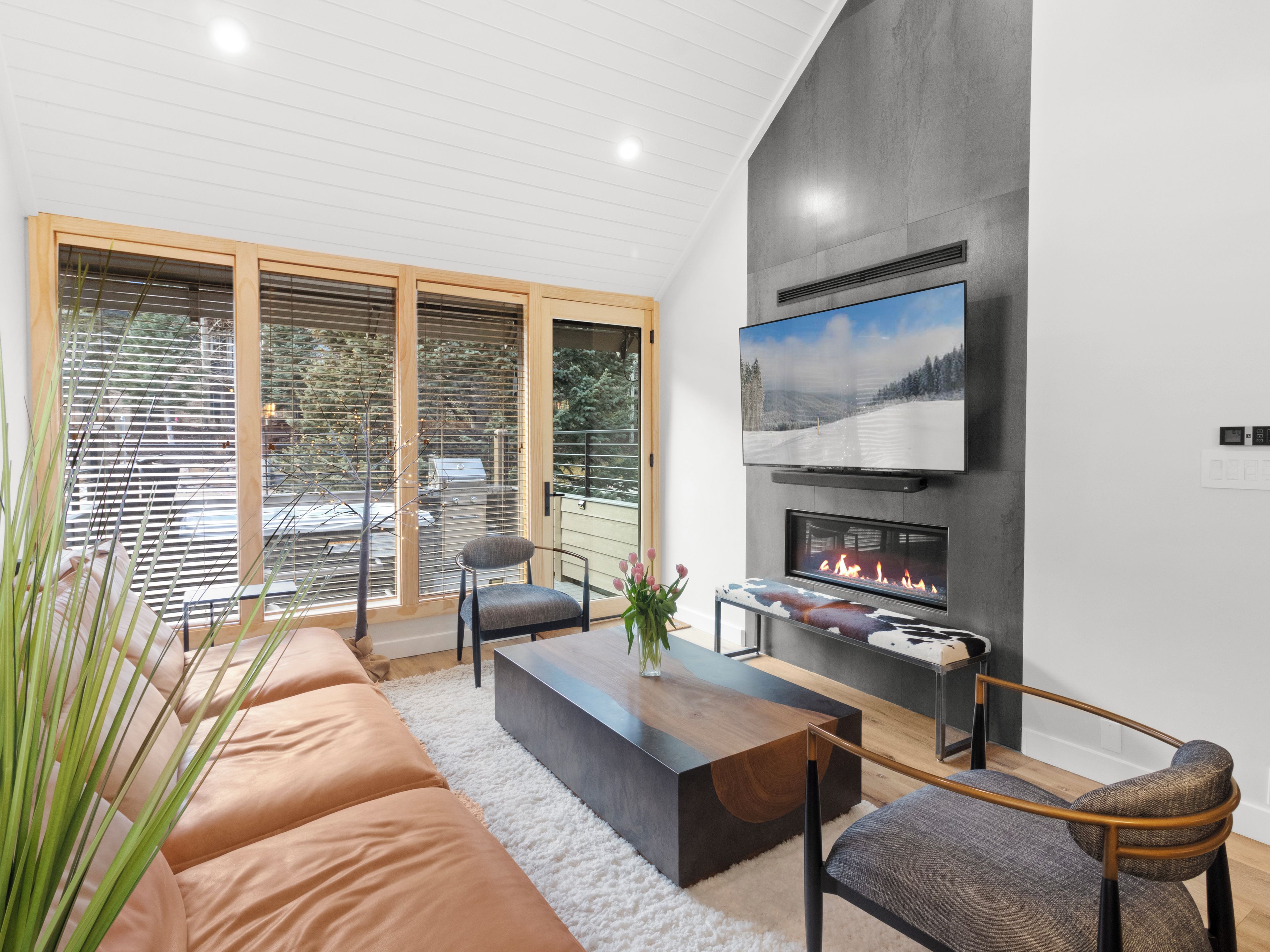 Ein modernes Wohnzimmer mit Kamin, einem an der Wand montierten Fernseher und einem großen Fenster mit Jalousien.