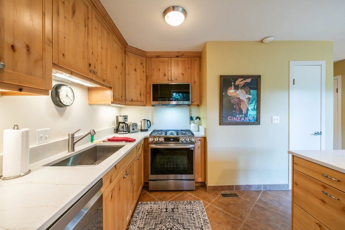 A kitchen with wooden cabinets, a stainless steel stove, a microwave, and a clock on the wall.
