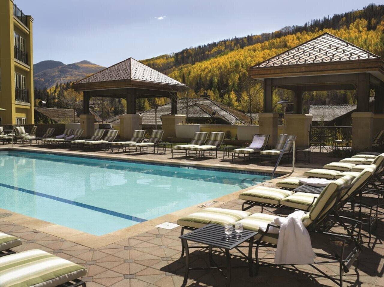 A pool area with lounge chairs and gazebos, surrounded by mountains and autumn foliage.