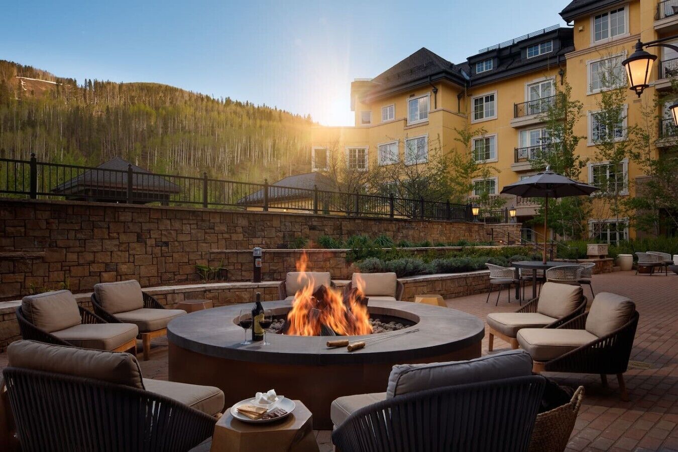 A circular outdoor seating area with a fire feature, surrounded by wicker chairs and a stone wall.