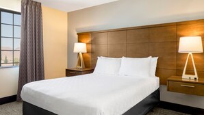 Een hotelkamer met een groot bed, twee nachtkastjes met lampen, een raam met gordijnen en een houten hoofdeinde.