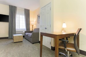 A hotel room with a desk, chair, sofa, and a window with curtains.