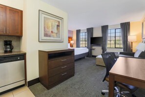 A hotel room with a kitchenette, a bed, a desk, and a chair.