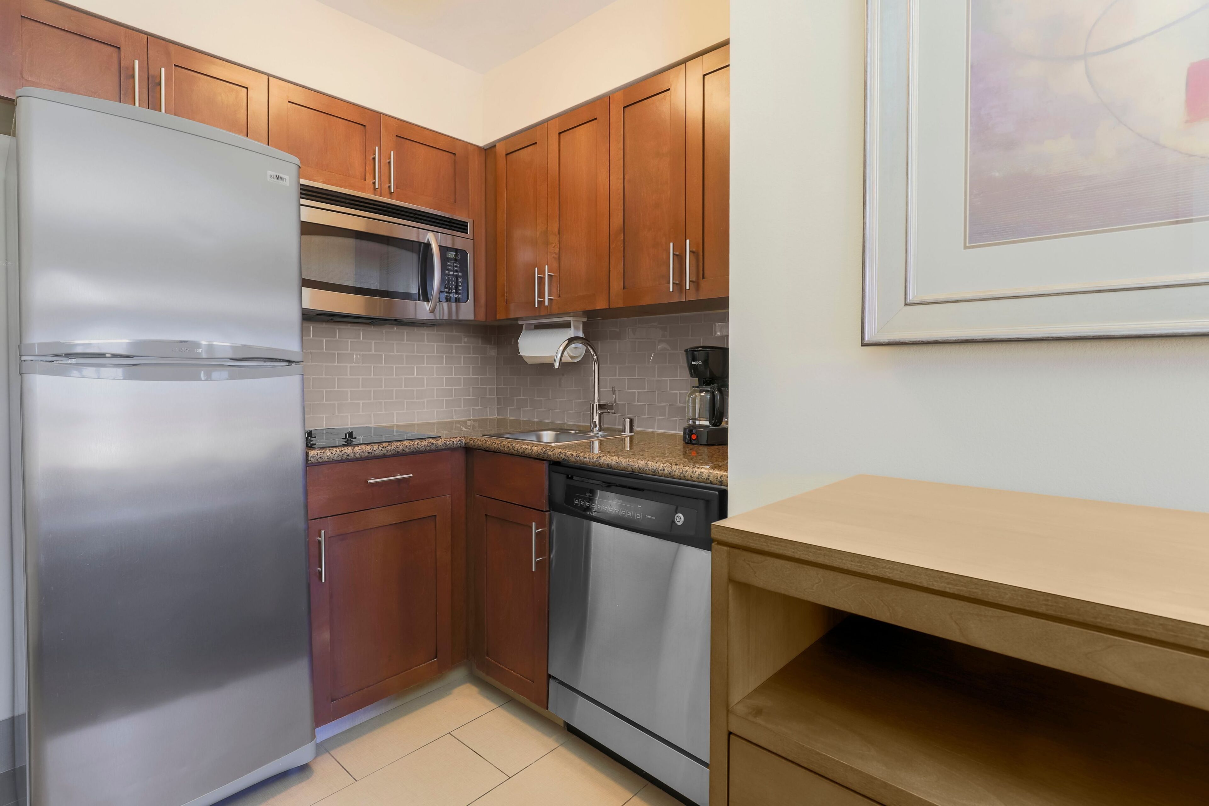 A compact kitchen with stainless steel appliances, wooden cabinets, and a tiled backsplash.
