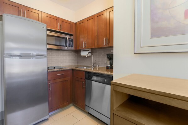 A compact kitchen with stainless steel appliances, wooden cabinets, and a tiled backsplash.