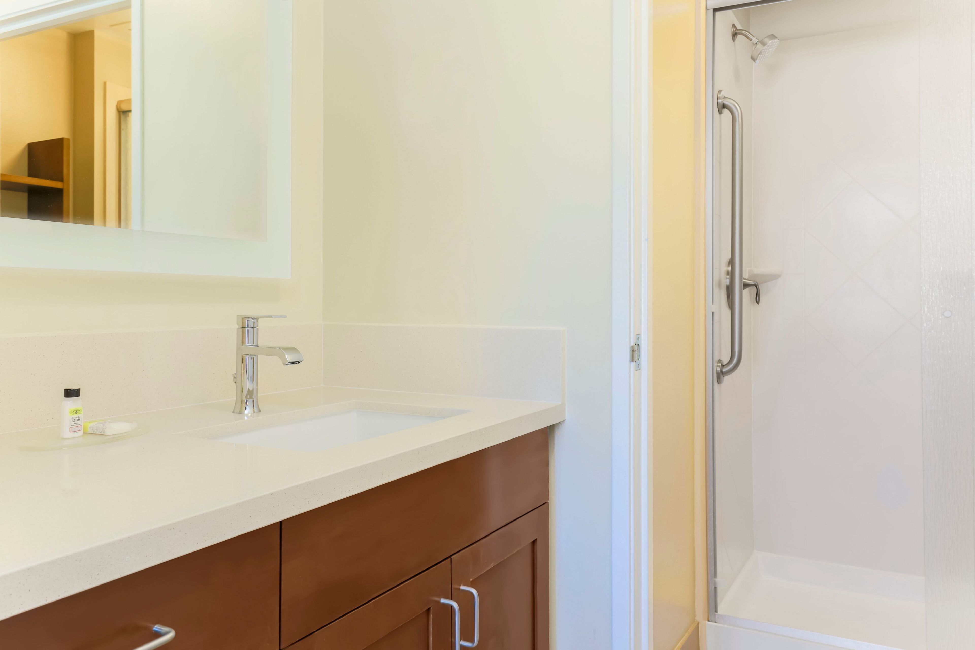 Een badkamer met een wit wastafelmeubel, een spiegel, een douche met glazen deur en bruine kastjes.