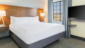 Ein Hotelzimmer mit einem großen Bett, zwei Nachttischlampen, einem Flachbildfernseher und einem Fenster mit Vorhängen.