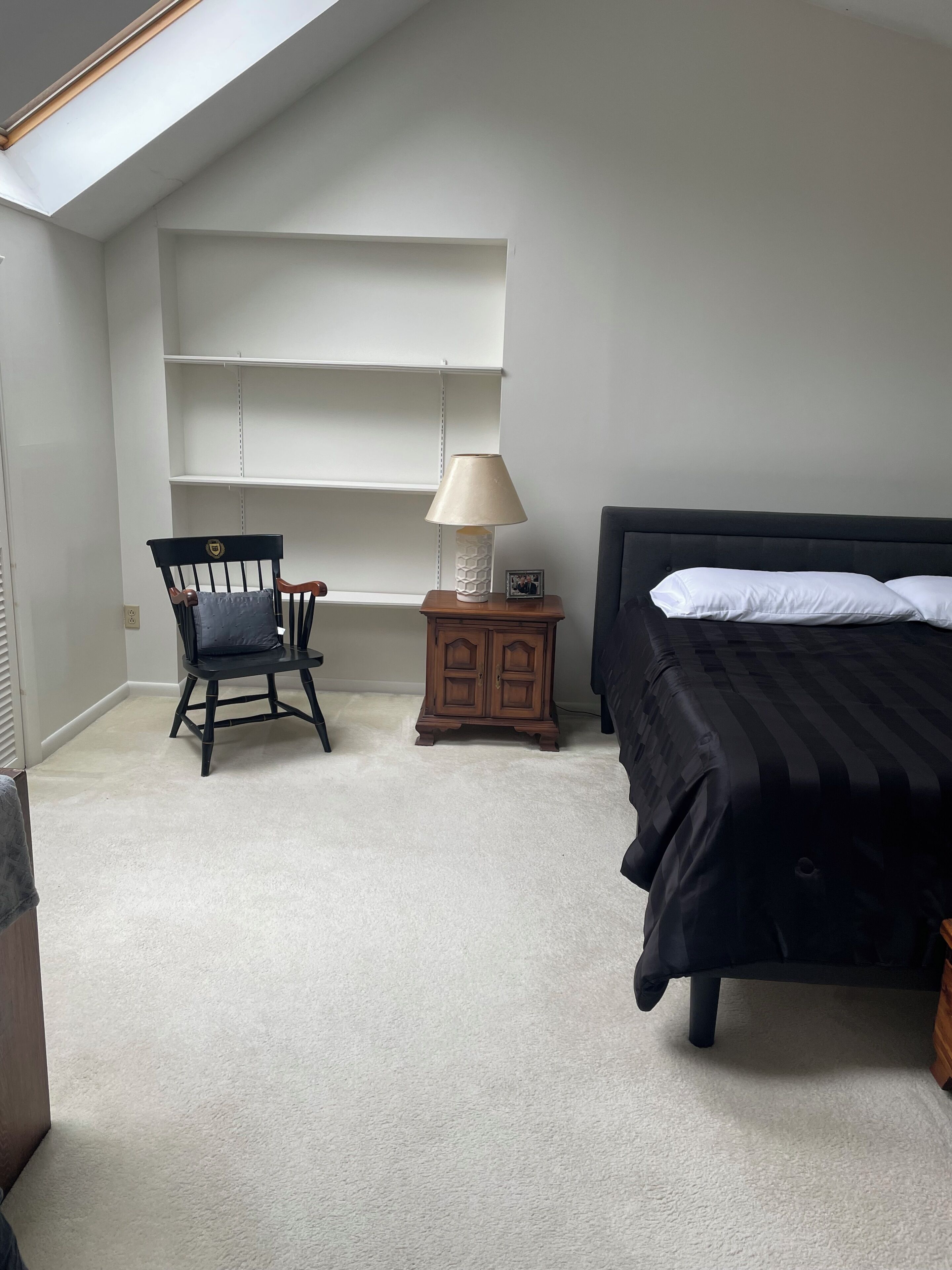 Ein Schlafzimmer mit einem Bett, einem Sessel, einem Nachttisch mit Lampe und einem Kleiderschrank.