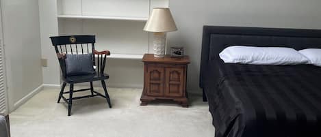 Un dormitorio con cama, una silla, una mesita de noche con lámpara y un armario.