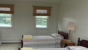 Et soveværelse med to senge, et natbord, en lampe og vinduer med persienner.