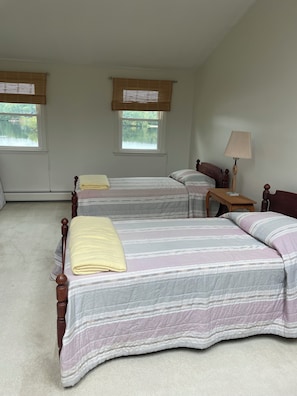 Un dormitorio con dos camas, una mesita de noche, una lámpara y ventanas con persianas.