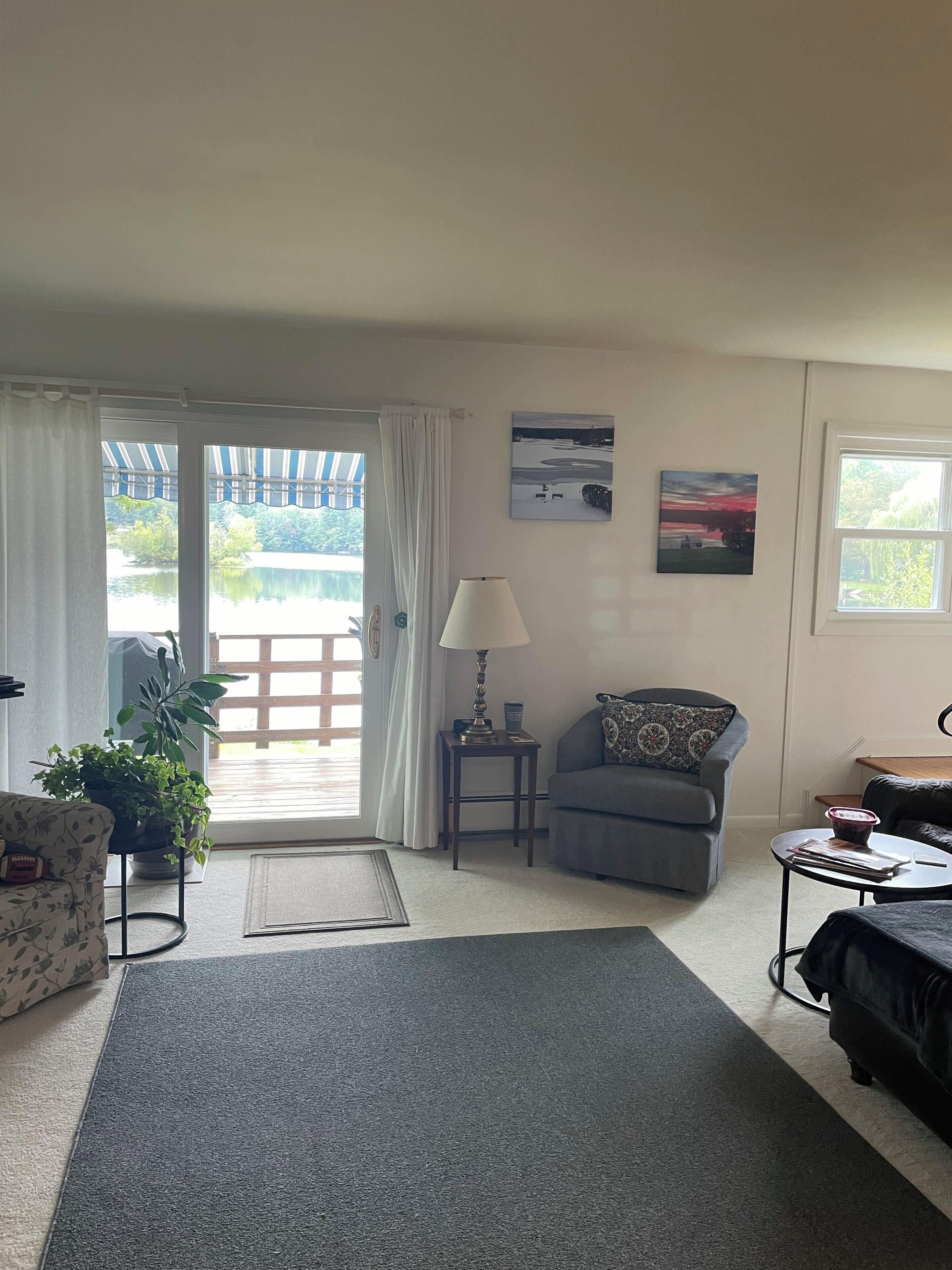 A living room with a sofa, a chair, a lamp, and a view of a lake through a glass door.