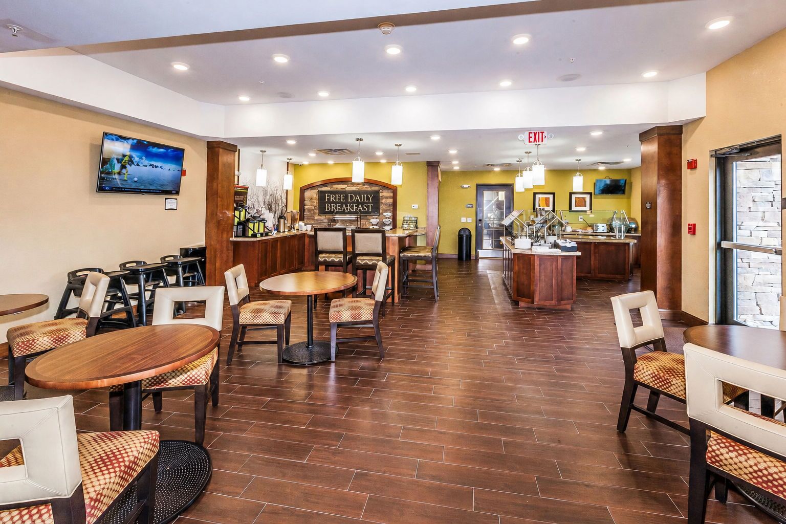 A hotel restaurant with multiple seating areas, a bar, and a television screen displaying a sports event.