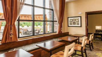 A hotel room with a large window, a wooden bench, and a dining area with tables and chairs.