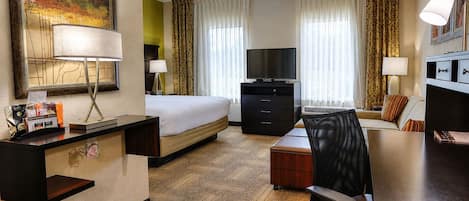A hotel room with a bed, desk, chair, television, and a painting on the wall.