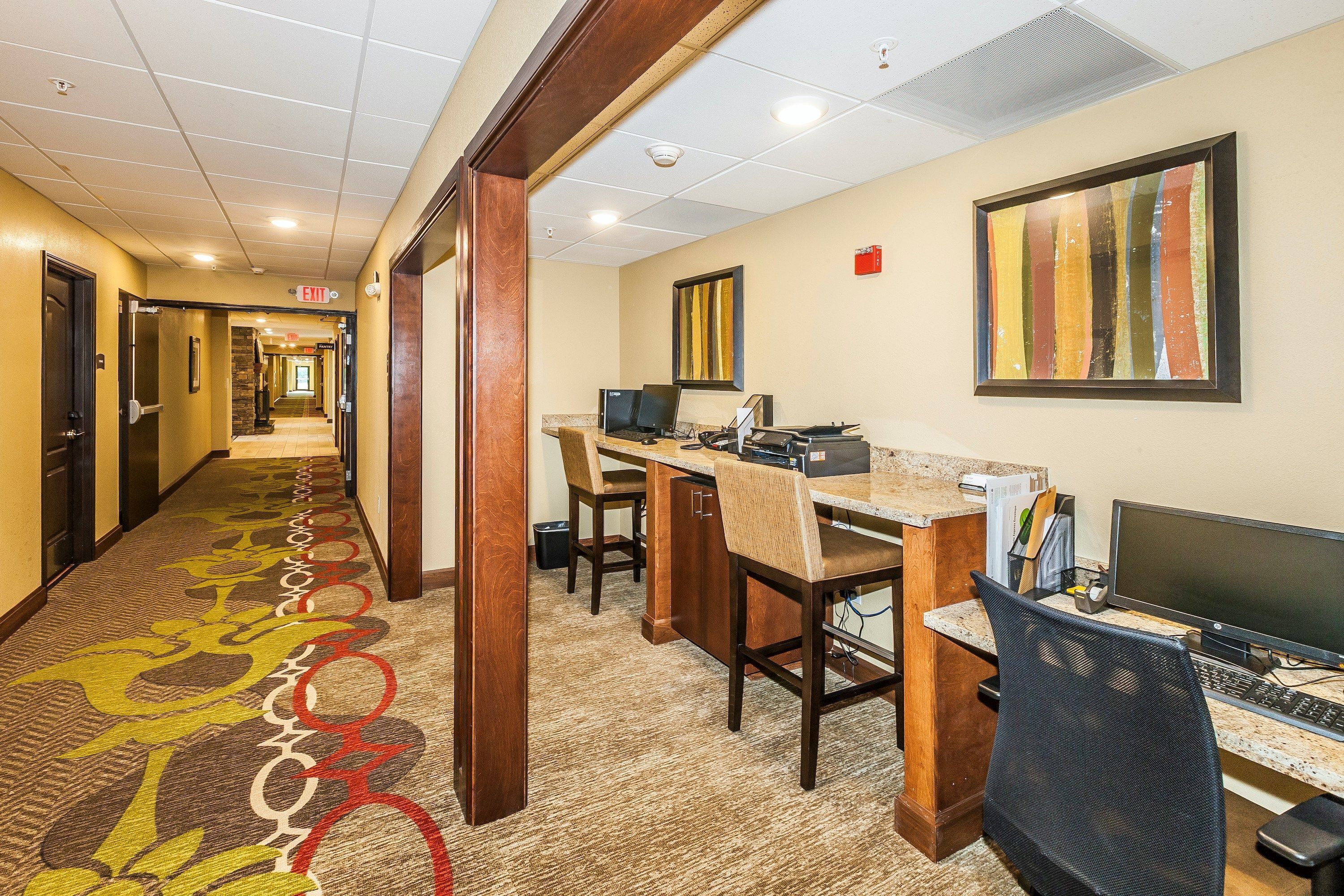 A hotel lobby with a carpeted hallway, a reception desk, computers, and a framed artwork on the wall.