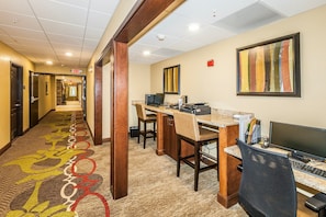 A hotel lobby with a carpeted hallway, a reception desk, computers, and a framed artwork on the wall.