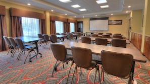 A conference room with a large table, multiple chairs, a projector screen, and a carpeted floor.
