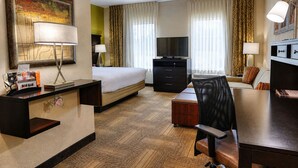 A hotel room with a bed, desk, chair, television, and a painting on the wall.
