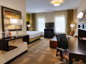 A hotel room with a bed, desk, chair, television, and a painting on the wall.