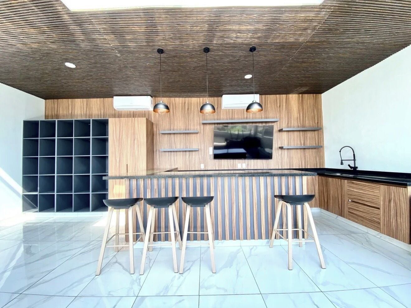 A modern kitchen with a wooden ceiling, a central island with stools, and a built-in TV.