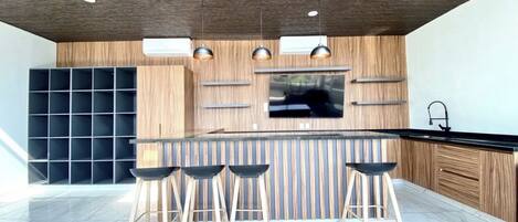 A modern kitchen with a wooden ceiling, a central island with stools, and a built-in TV.
