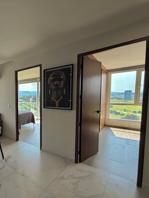A room with a bed, a framed artwork, and a door leading to a balcony with a city view. - Agave House | Panoramic View | Near Andares and Hospitals (Zapopan)