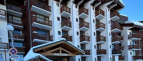 A multi-story hotel with balconies, a ski lift, and a sign indicating 'LES HAMEAUX 1'.