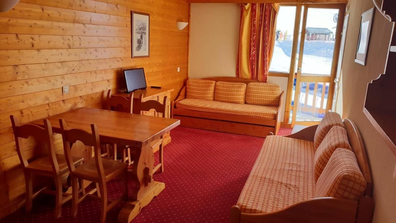 Et hyggeligt rum med træpaneler, et spisebord med stole, en sofa og et vindue med gardiner.