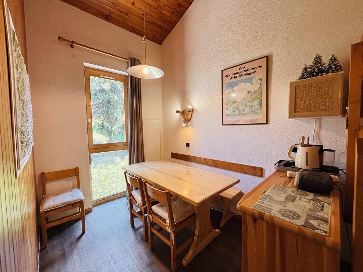 A cozy dining area with a wooden table and chairs, a bench, a hanging light fixture, and a framed picture on the wall.