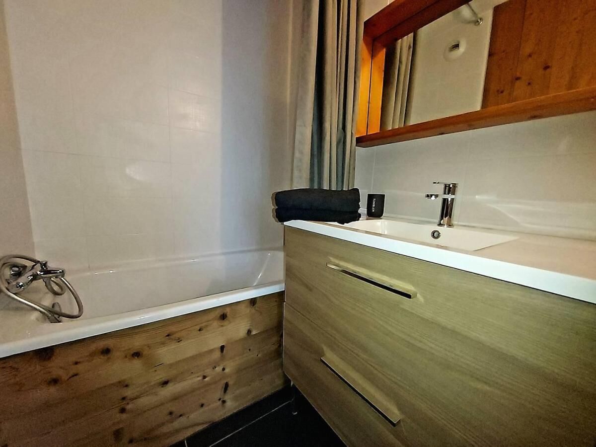 A bathroom with a bathtub, wooden paneling, a sink, and a mirror.