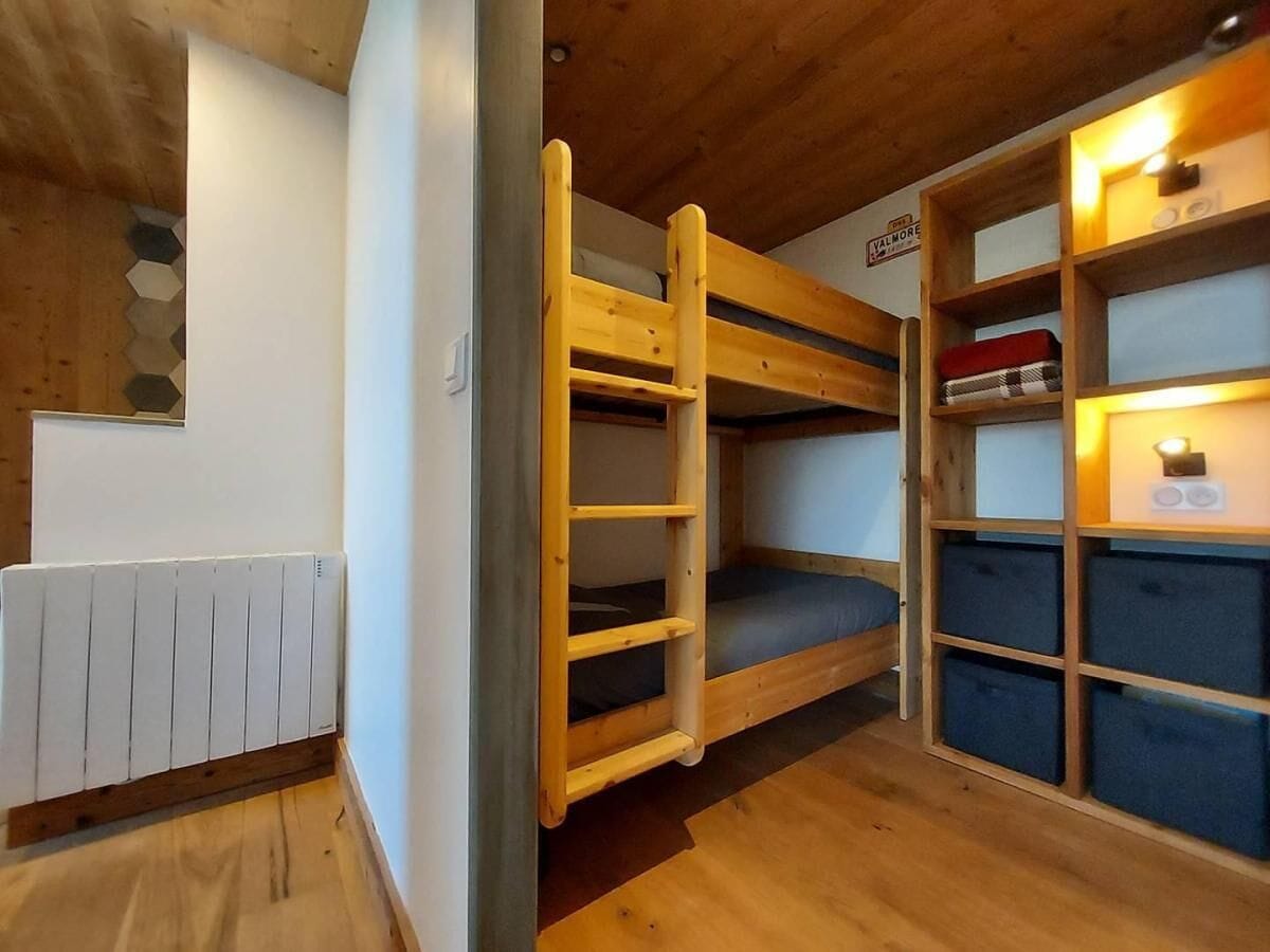Un lit superposé avec une échelle, un radiateur et une étagère avec des boîtes de rangement.