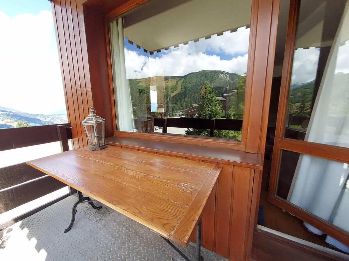 A wooden table with a metal frame, a glass lantern, and a view of a mountain landscape through a window.