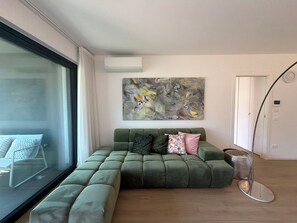 A modern living room with a sectional sofa, a large abstract painting, and a glass door leading to a balcony. - CasaRipa, one-bedroom apartment with olive grove view, 5 minutes from the lake (Riva del Garda)