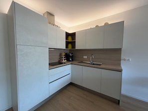 A modern kitchen with white cabinetry, a wooden countertop, and a built-in coffee maker. - CasaRipa, one-bedroom apartment with olive grove view, 5 minutes from the lake (Riva del Garda)