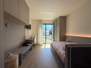 A hotel room with a bed, a desk, a chair, a television, and a view of the outdoors. - CasaRipa, one-bedroom apartment with olive grove view, 5 minutes from the lake (Riva del Garda)