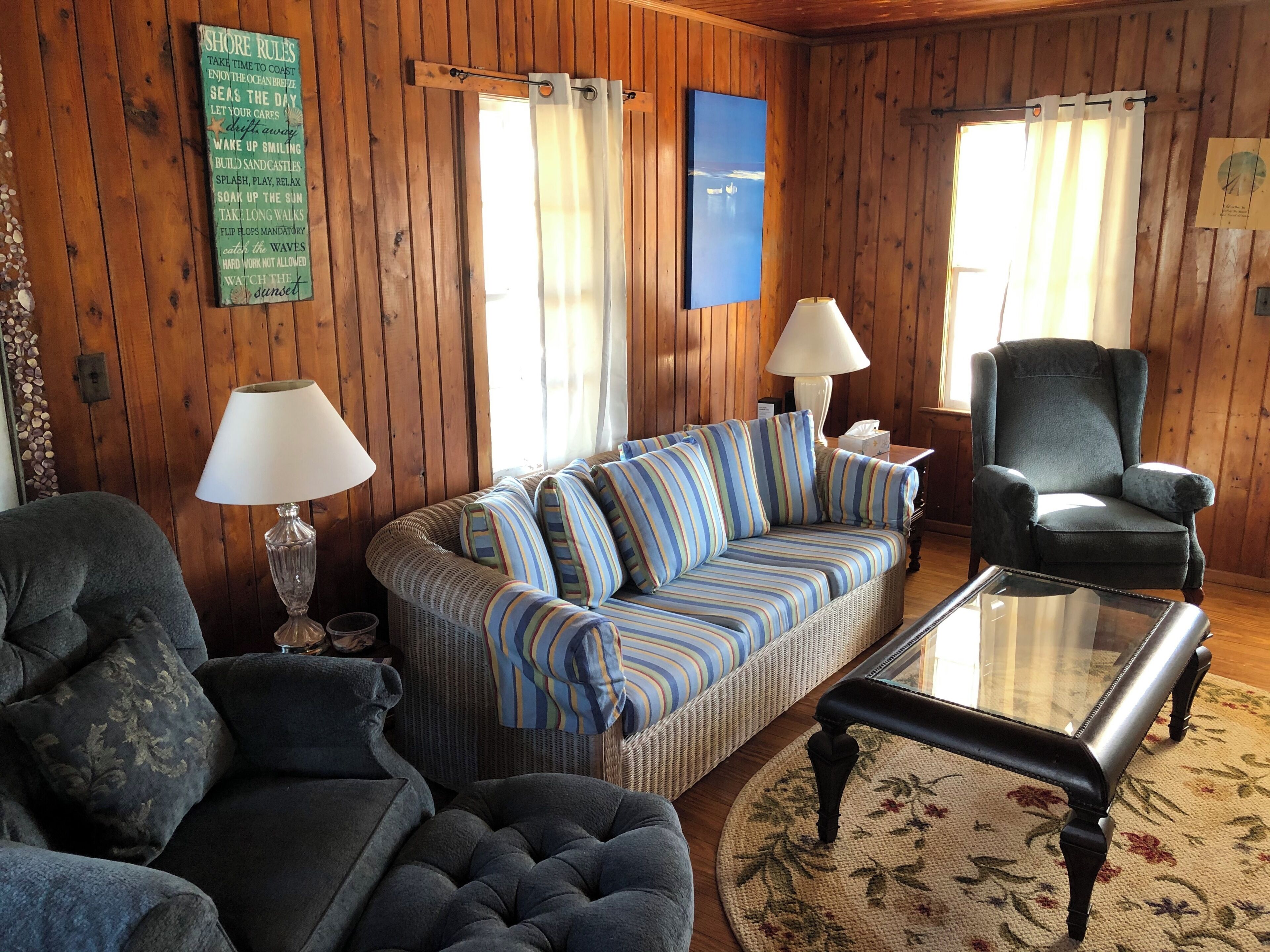 A cozy living room with a sofa, armchairs, a coffee table, and a wooden wall with a sign.