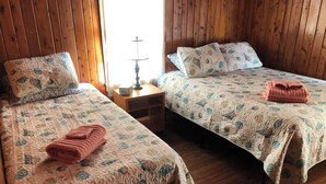 Two beds with floral bedding, wooden headboards, and a nightstand with a lamp between them. - 2-bedroom cottage with AC in welcoming Kitty Hawk (Kitty Hawk)
