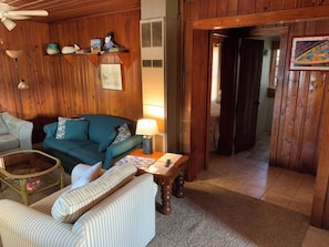Ein gemütliches Wohnzimmer mit einer Couch, einem Couchtisch und einer Lampe. Eine Tür führt in einen anderen Raum.