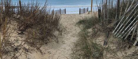 A sandy beach path leading to the sea with a wooden fence on the right.