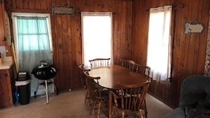 A wooden-paneled room with a dining table and chairs, a grill, and a sign reading 'AT THE BEACH'. - 2-bedroom cottage with AC in welcoming Kitty Hawk (Kitty Hawk)