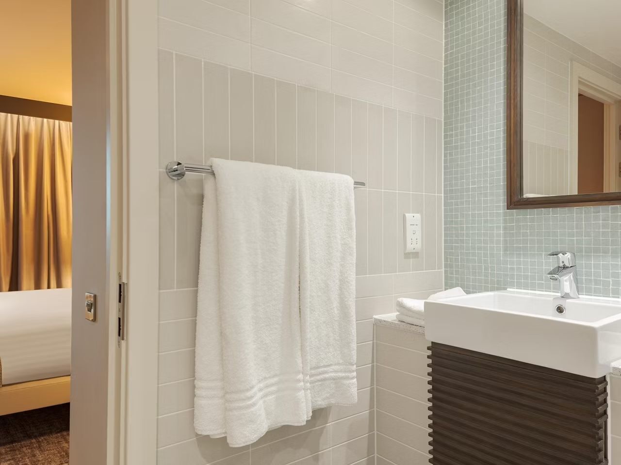 Un bagno d'hotel con un lavandino bianco, un asciugamano appeso a un porta asciugamani e uno specchio sopra il lavandino.