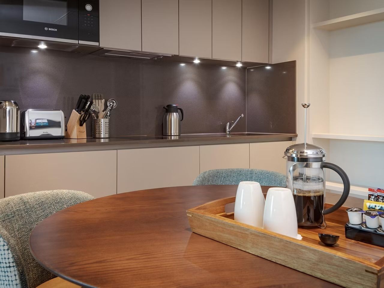 A modern kitchen with a Bosch microwave, a coffee maker, and a dining table with a tray of cups and a coffee pot.