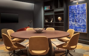 Una sala de conferencias moderna con una mesa redonda, seis sillas, un cuadro abstracto de gran tamaño y una estantería con premios.