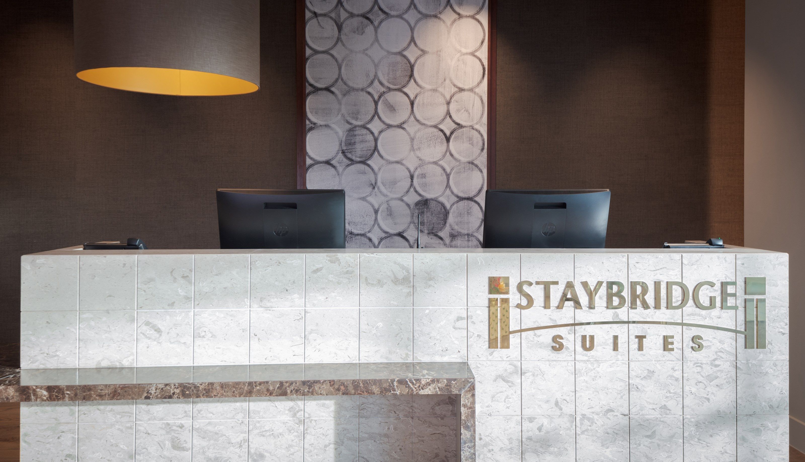A reception desk with two laptops, a lamp, and a wall with circular patterns.