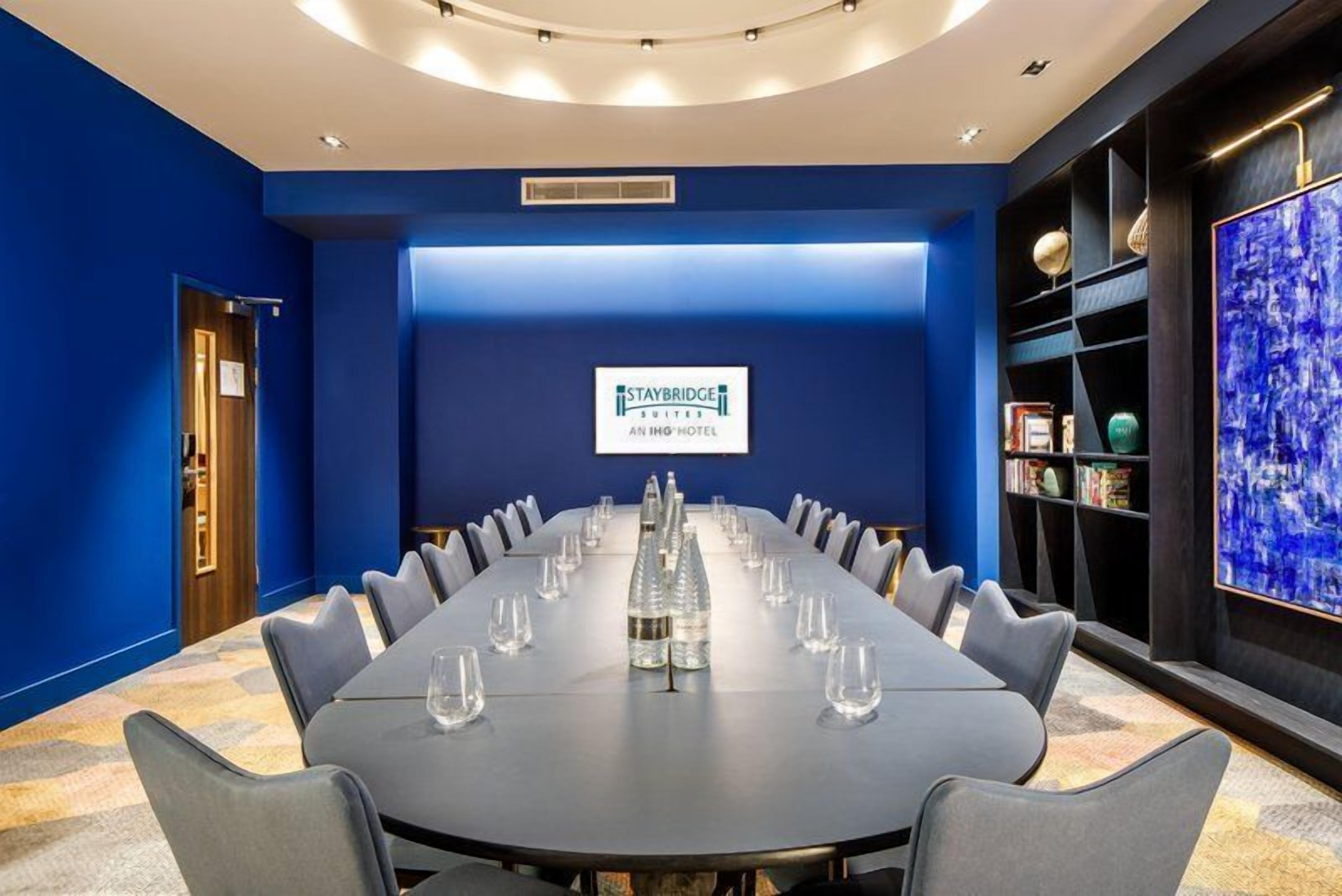 A conference room with a long table, chairs, and a blue wall with a logo.