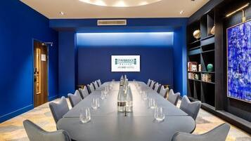 A conference room with a long table, chairs, and a blue wall with a logo.