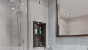 Une salle de bain moderne dotée d’une douche à parois de verre, d’un meuble à pharmacie encastré et d’un grand miroir au-dessus du lavabo.
