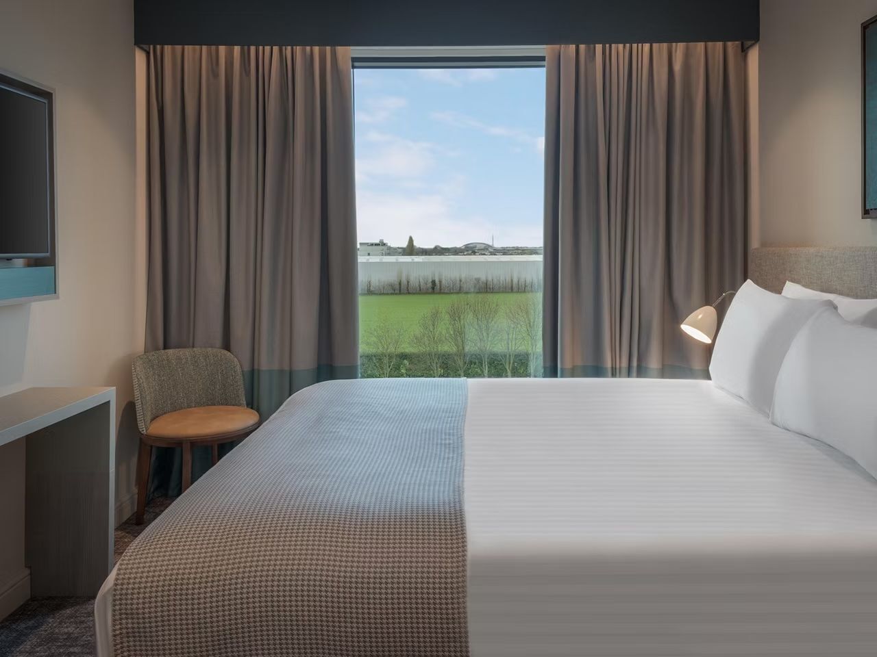 A hotel room with a large bed, a desk, a chair, and a view of a body of water.