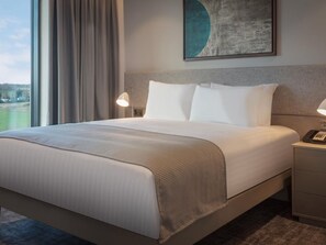 A hotel room with a large bed, a bedside table with a lamp, a phone, and a painting on the wall.